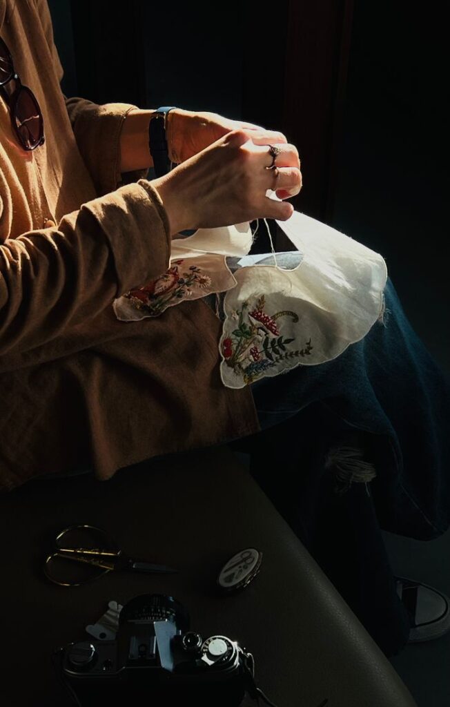 Woman's hands embroidering fabric with intricate design in natural light, highlighting skilled craftsmanship.