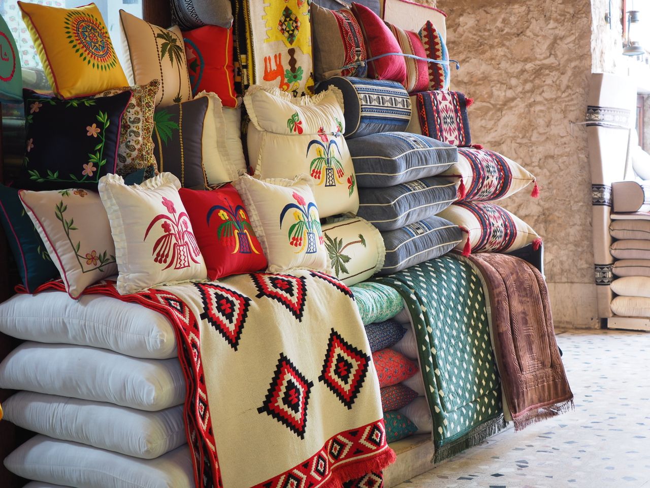 The Art of Drawing Readers In: Your attractive post title goes here Vibrant embroidered cushions and textiles on display in a Doha market.