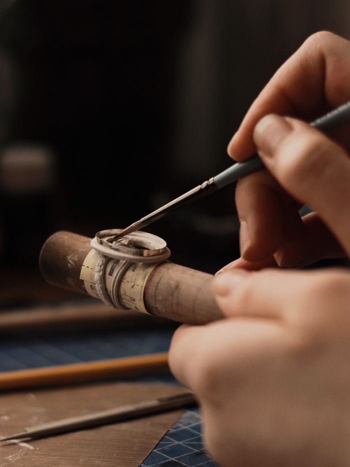 Close-up of a jeweler's hand crafting silver rings with tools in a workshop setting.